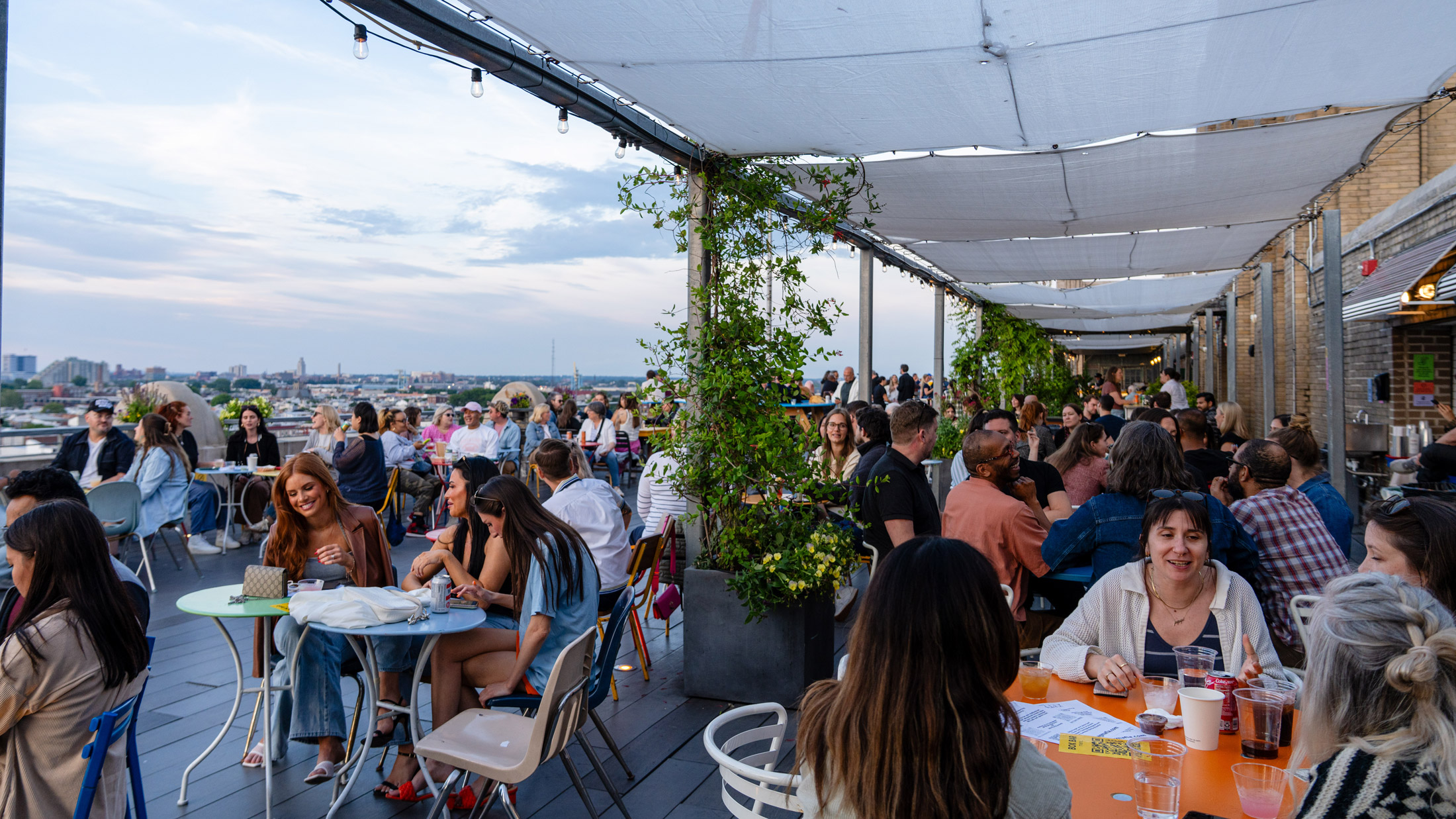 People sit and enjoy drinks at the Bok Bar in South Philly, with a view of the city in the background.