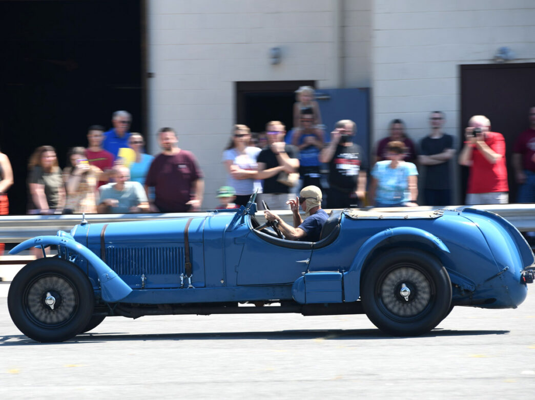 A retro-style blue car being driven at a demo day at Simeone Foundation Automotive Museum.