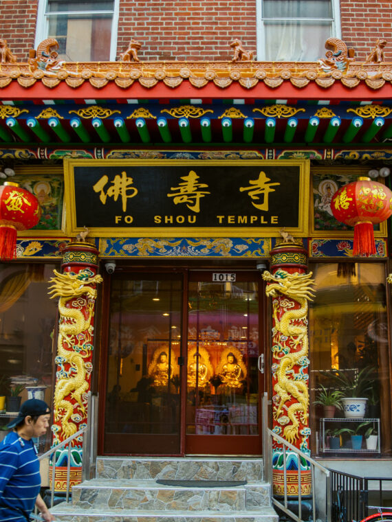 The ornately decorated entrance to Fo Shou Temple in Philadelphia's Chinatown features traditional Chinese architectural elements including curved eaves, golden dragons, red lanterns, and elaborately carved pillars with traditional designs.
