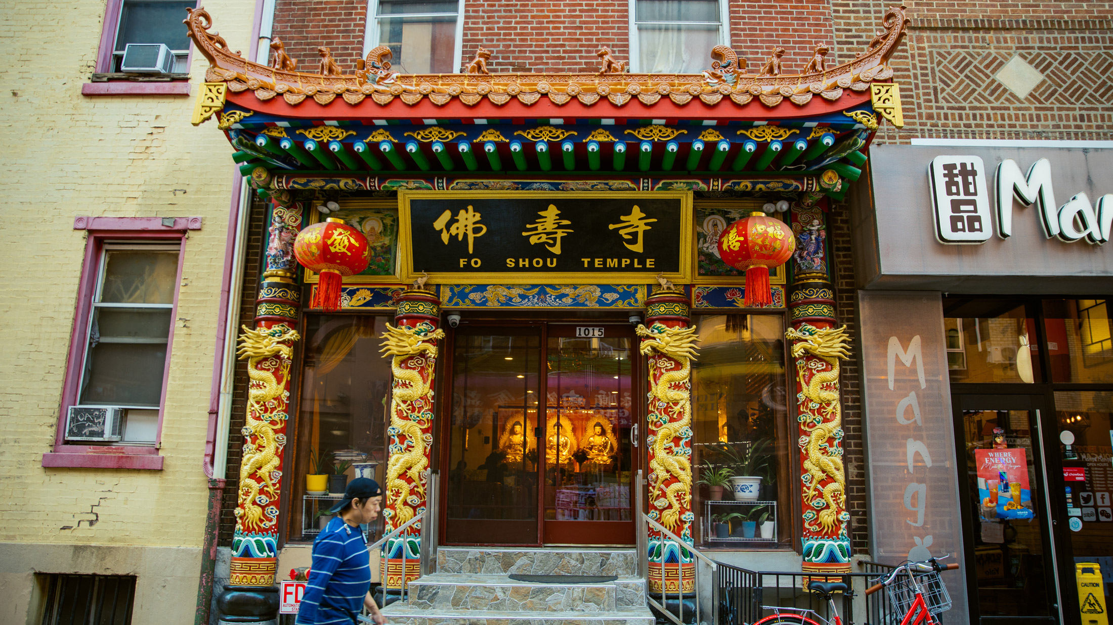 A entrada ornamentada do Fo Shou Temple no Chinatown da Filadélfia apresenta elementos arquitetônicos chineses tradicionais, incluindo beirais curvos, dragões dourados, lanternas vermelhas e pilares elaboradamente esculpidos com desenhos tradicionais.