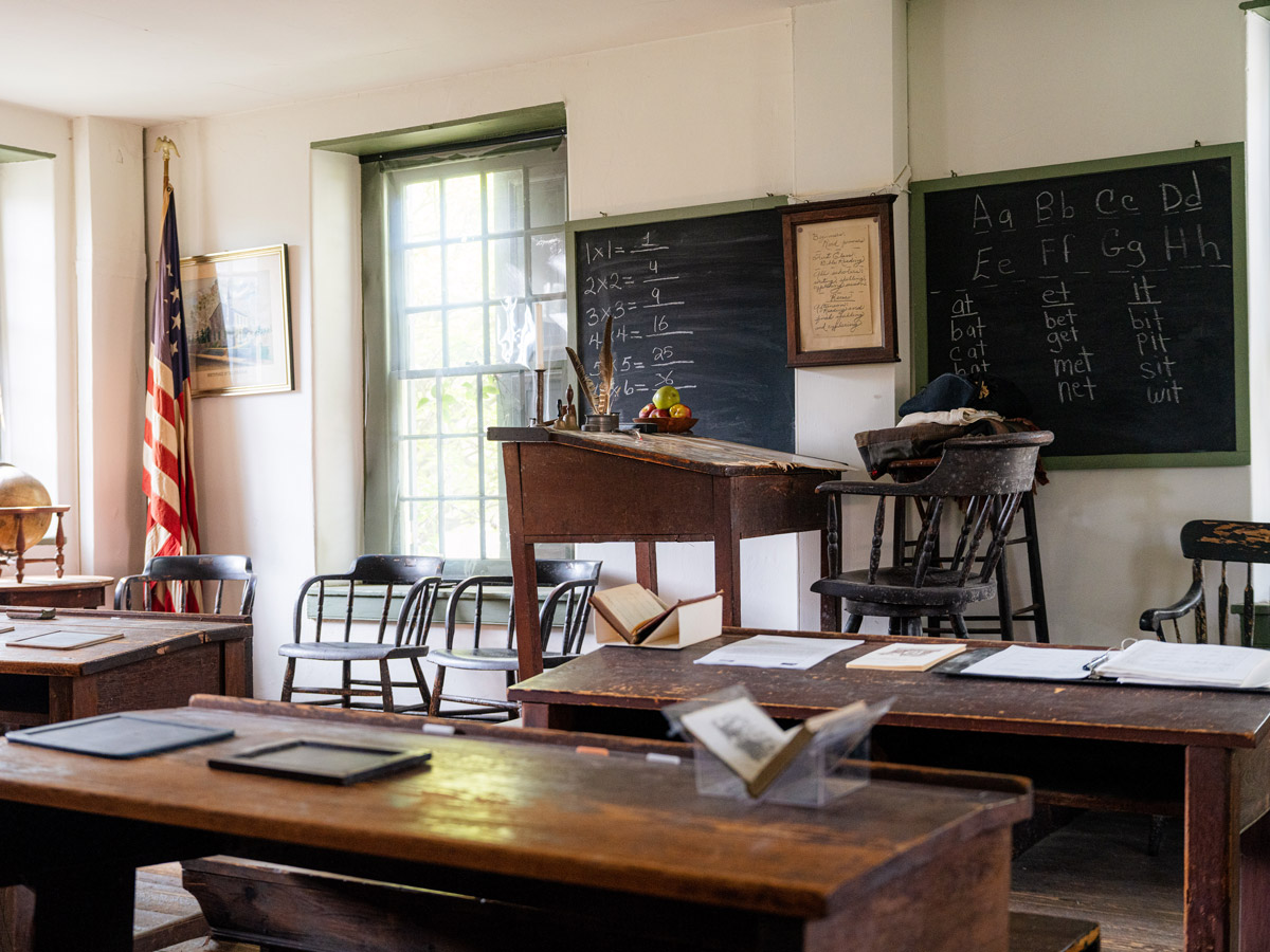 The preserved interior of the historic Concord School House in Germantown, Philadelphia, featuring wooden desks, chalk blackboards with multiplication tables and the alphabet, and an American flag.