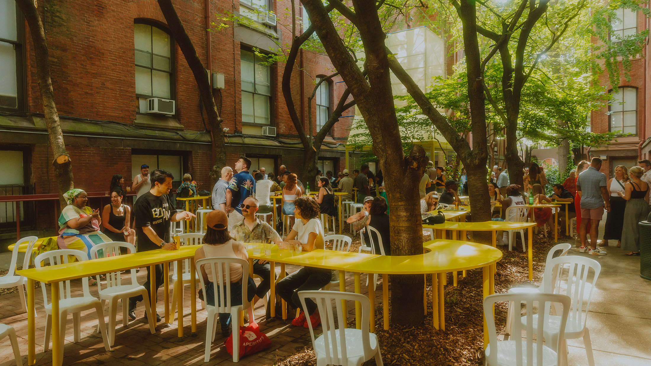 People sit around tree trunks while a yellow table wraps around a tree at Frankie's Summer Club in Philadelphia