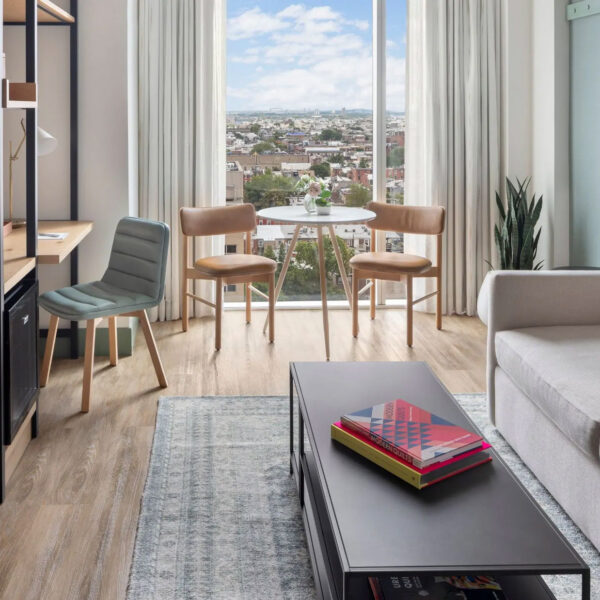 Modern guest room at Hyatt Centric Philadelphia featuring a light-filled seating area with a sofa, coffee table, and small dining set by a large window overlooking the city skyline.