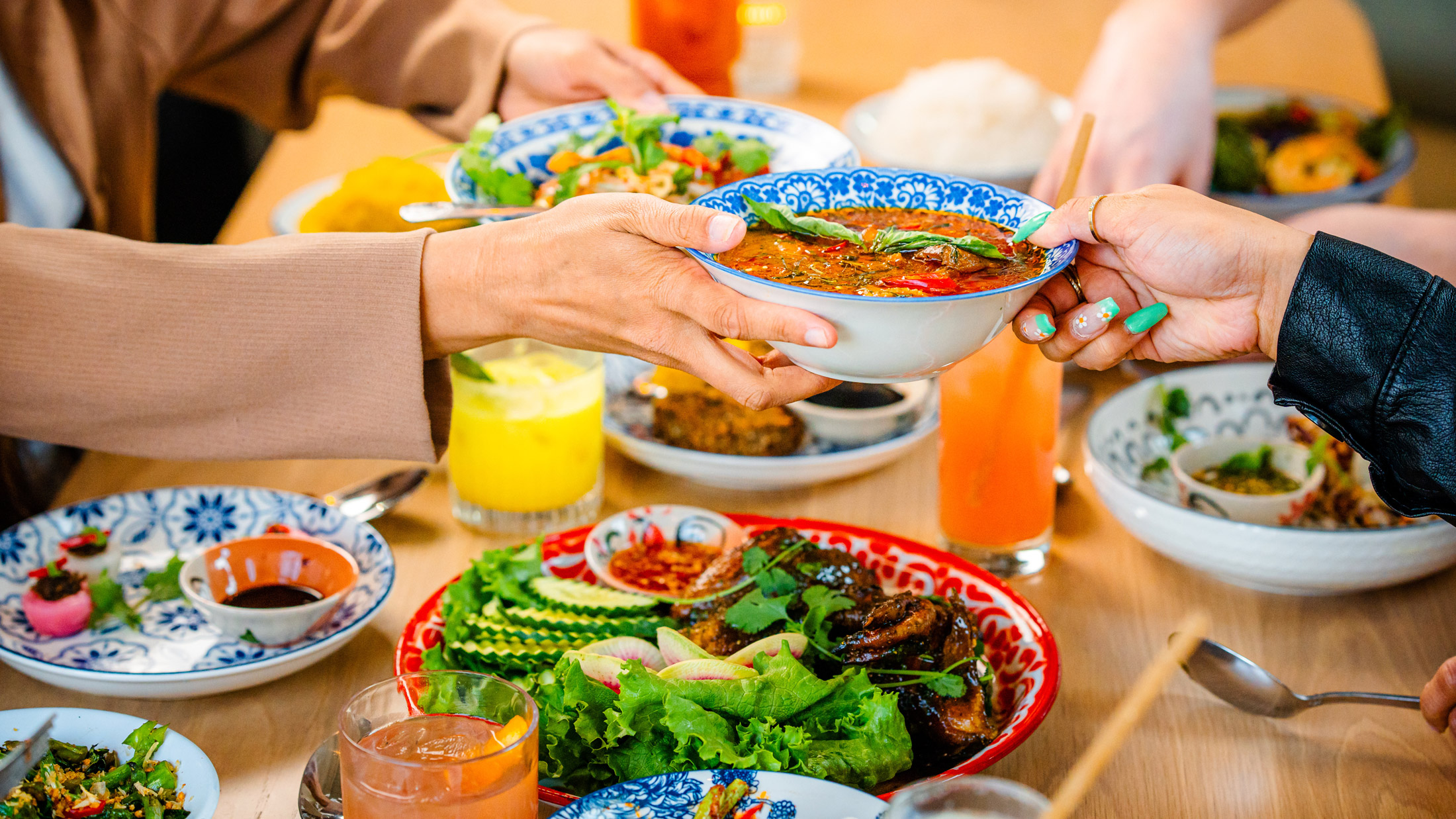Los comensales del restaurante Kalaya, en Filadelfia, se pasan un plato de curry tailandés de colores vivos a través de una mesa repleta de platos coloridos, hierbas frescas y cócteles de vivos colores.
