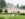 Visitors enjoying the fountains at Longwood Gardens, with a large ornate cream-colored pavilion building, dramatic water jets spraying in the background, manicured hedges, and tall evergreen trees framing the scene.