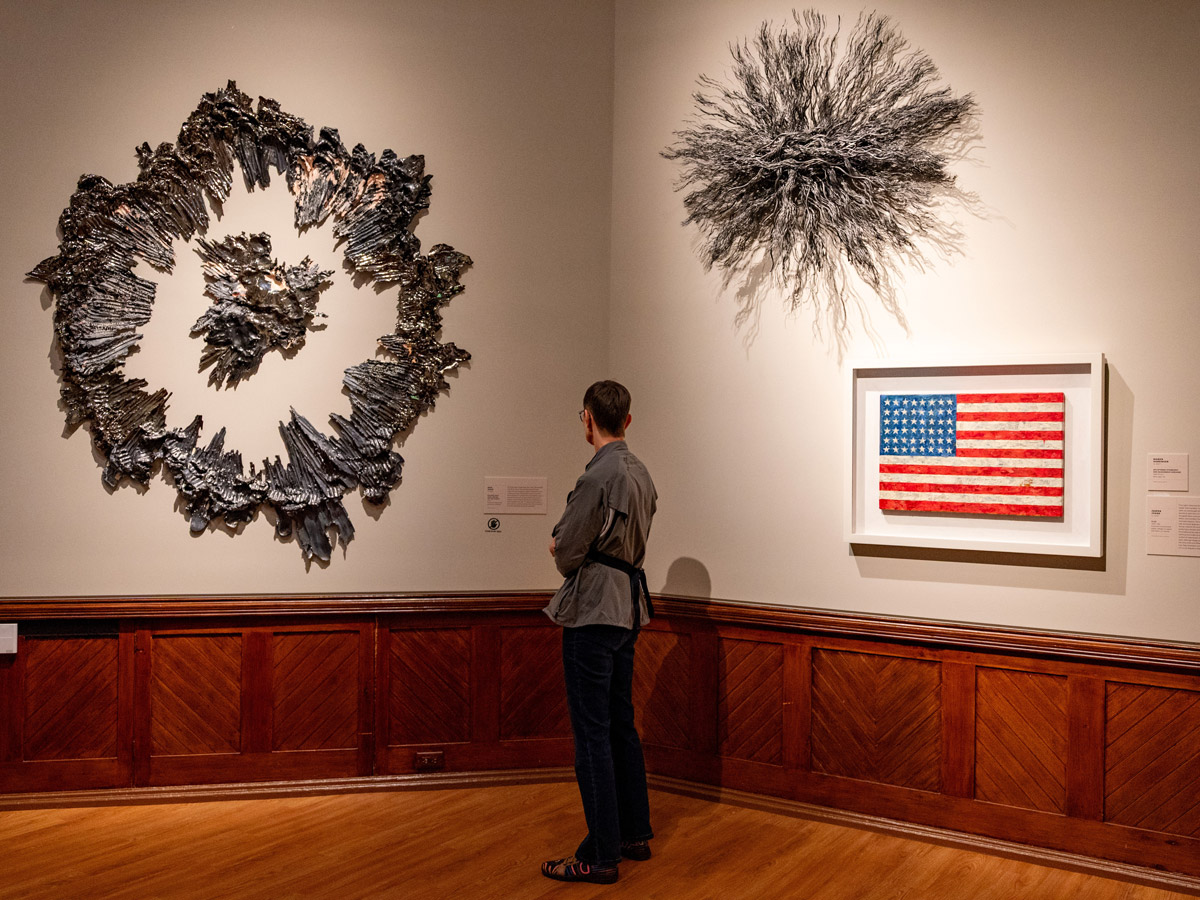 Visitor views contemporary artworks, including a sculptural metal wall piece and an American flag artwork, in the “A Nation of Artists” exhibit at the Pennsylvania Academy of the Fine Arts in Philadelphia.
