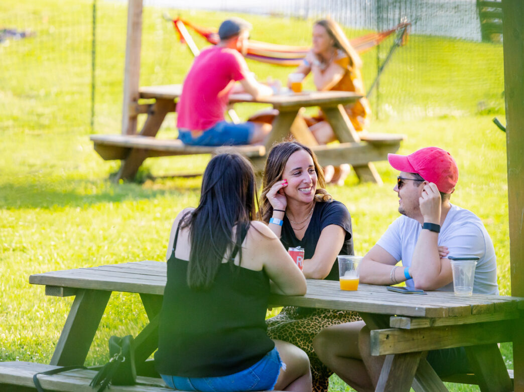Three people sit at a table over drinks at Parks on Tap at Azalea Garden in East Fairmount Park.