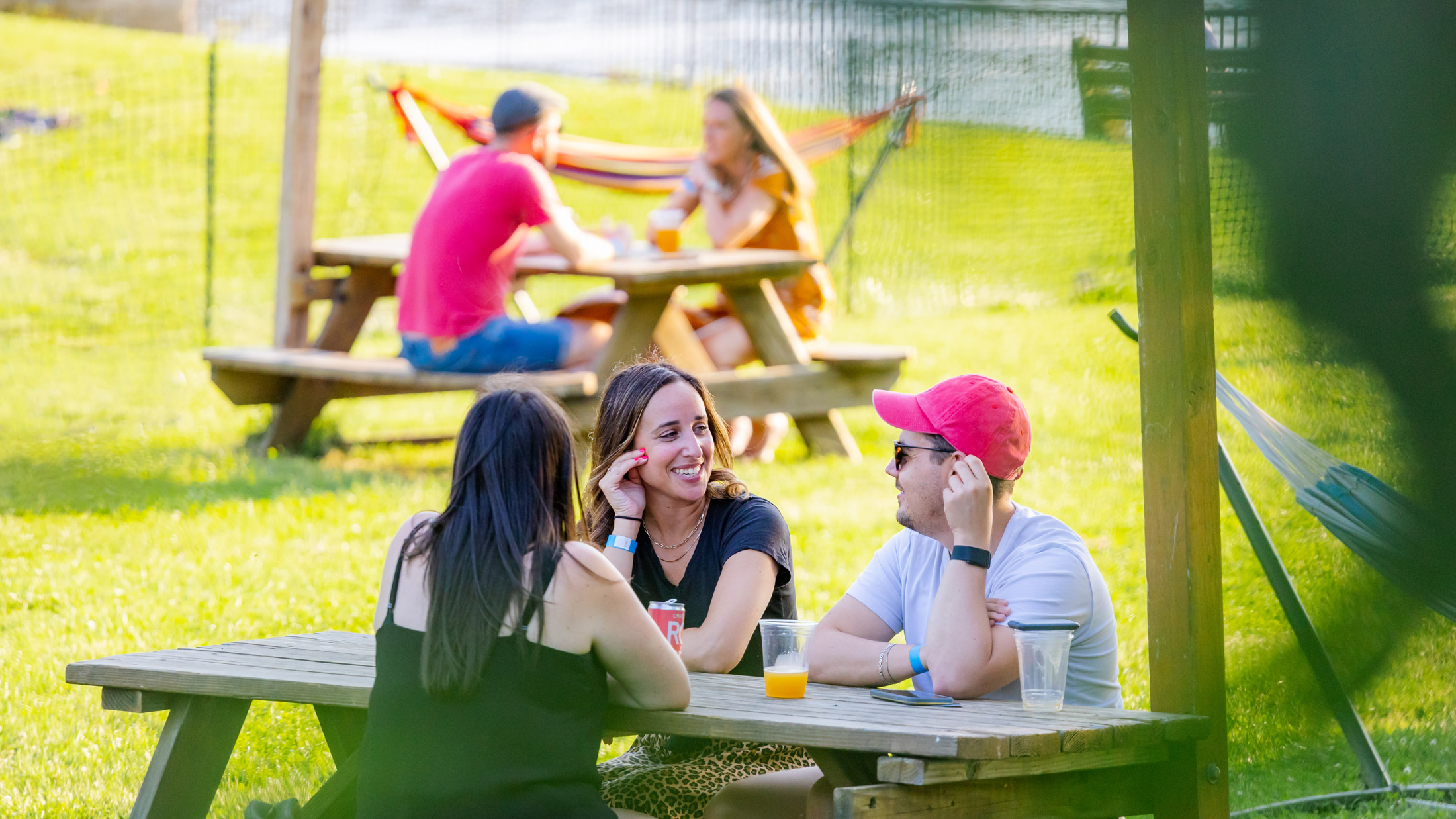 People sit outside and chat over drinks by the water during Parks on Tap at Azalea Garden.