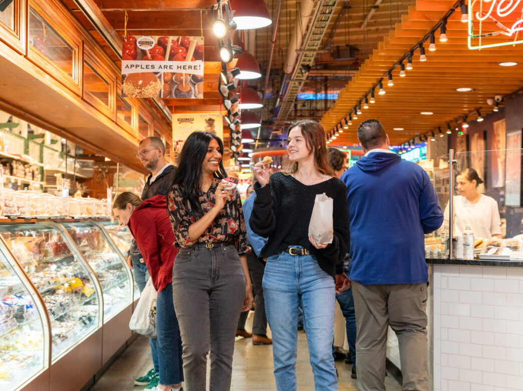 Two women walk together and eat baked goods at Reading Terminal Market.