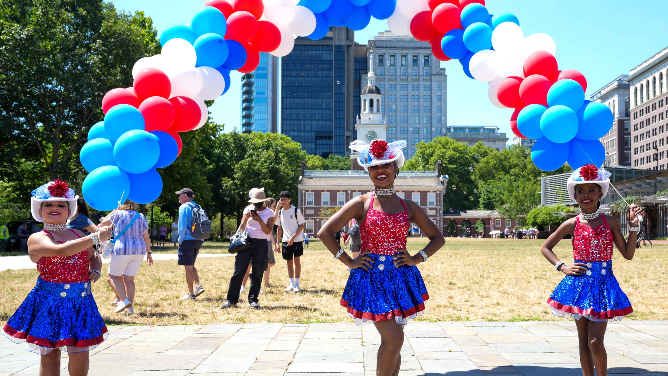Tres personas con atuendos patrióticos frente al Independence Hall durante el evento «Red White & Blue To Do».