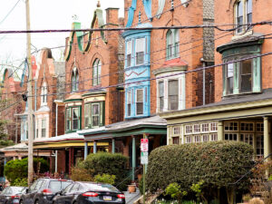 Een rij bakstenen Victoriaanse huizen met kleurrijke en sierlijke accenten staan langs een woonstraat in West Philadelphia.