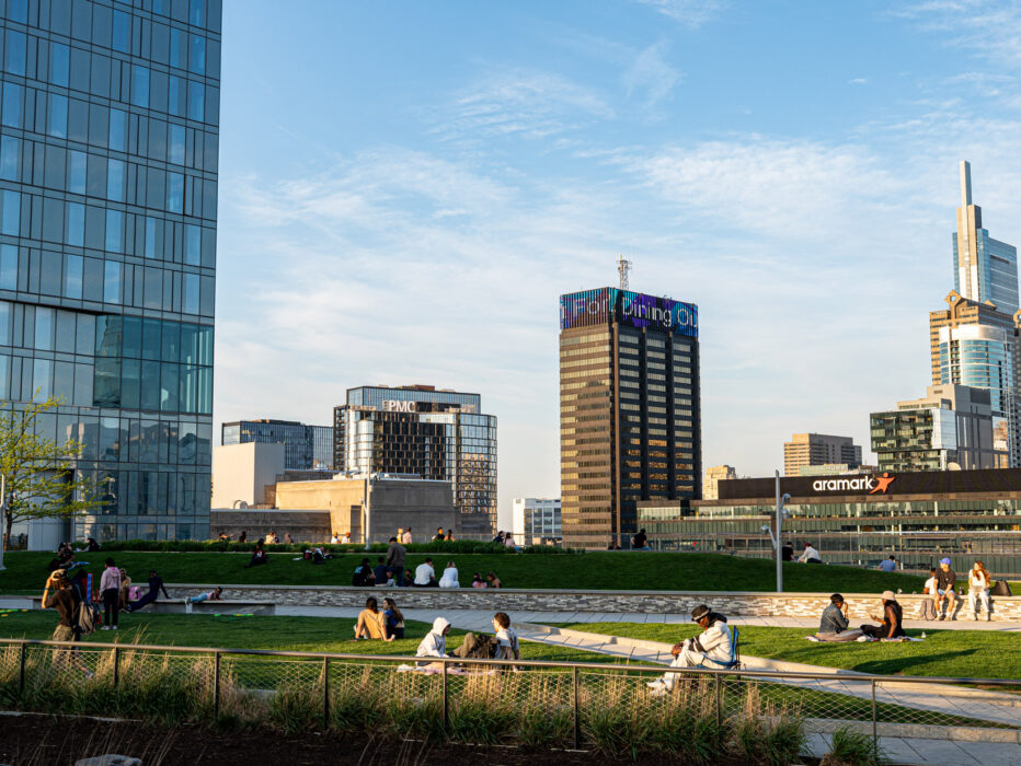 Les gens se rassemblent en groupes lors de la soirée Sunset Social au Cira Green, avec les gratte-ciel en arrière-plan.
