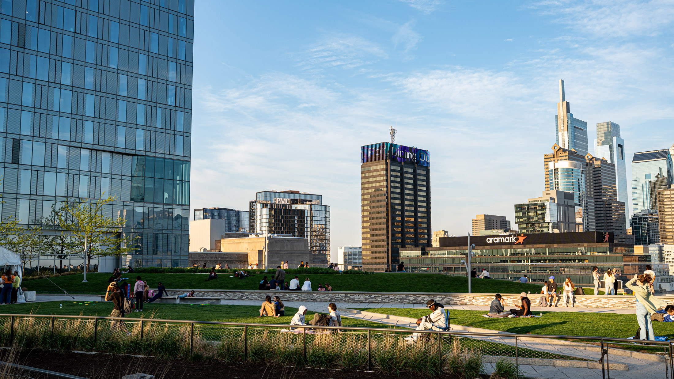 People gather in groups during Sunset Social at Cira Green with skyscrapers in the background.