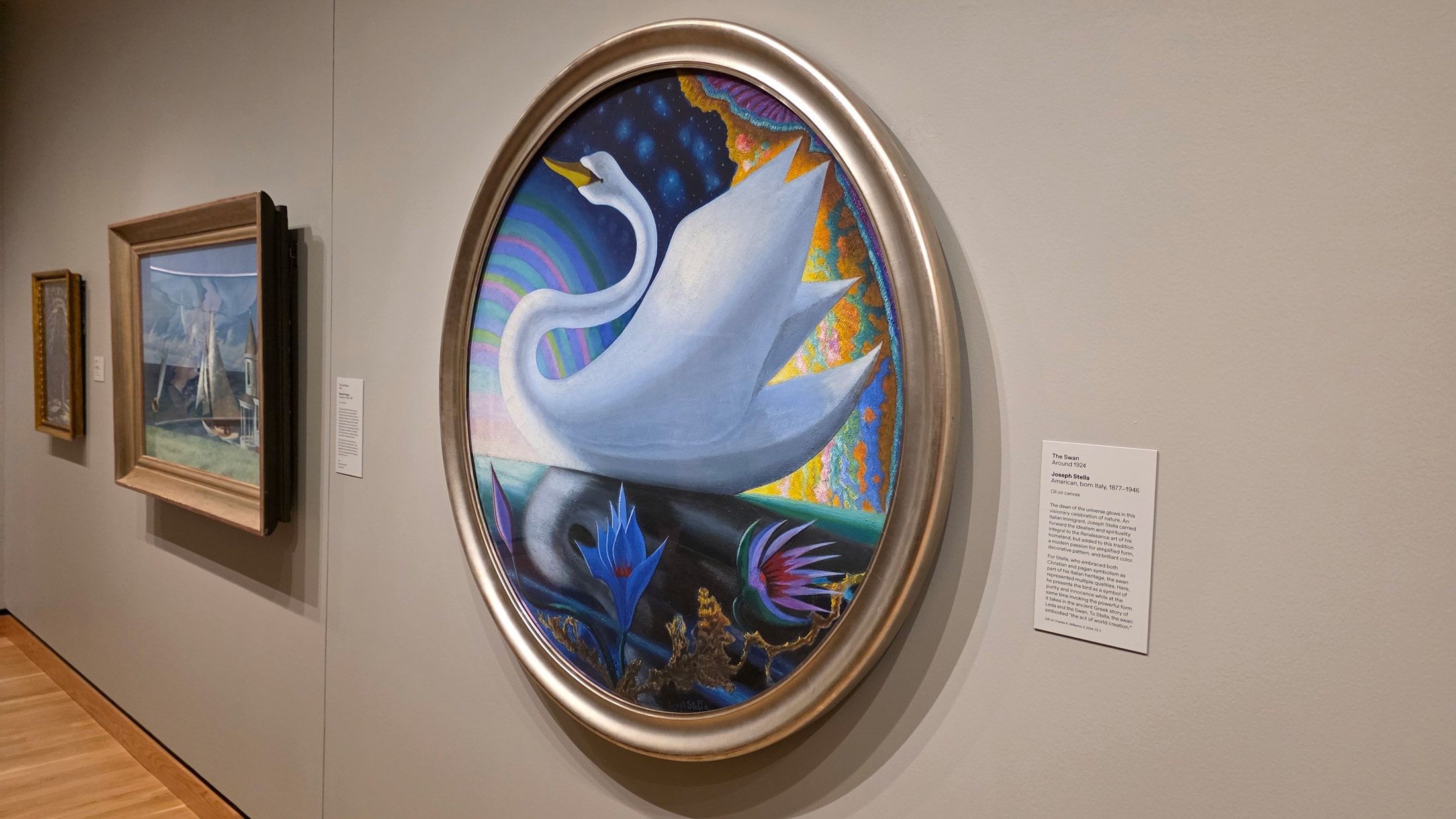 Oval-framed painting of a stylized white swan set against a colorful, dreamlike landscape hangs on a gallery wall in Philadelphia’s A Nation of Artists exhibit, with additional framed artworks displayed nearby.
