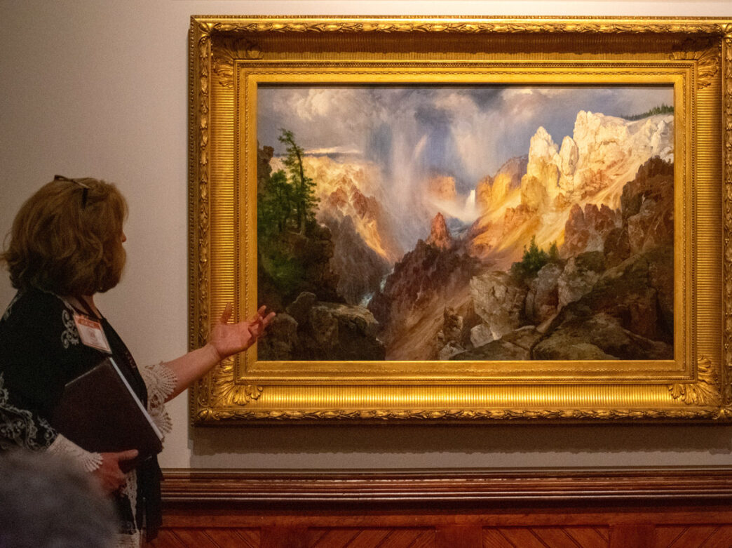 A woman gestures toward a large landscape painting in an ornate gold frame on display at the Pennsylvania Academy of the Fine Arts (PAFA) in Philadelphia.