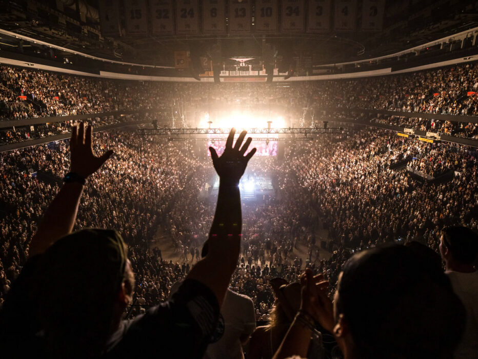 Crowd fills Xfinity Mobile Arena in Philadelphia during a concert, with thousands of fans cheering and raising their hands toward a brightly lit stage at center.