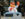 Gritty, Philadelphia Flyers mascot, holds a cup of coffee while waving. A tablecloth is draped over a trashcan in front of him, which is topped with a hoagie, chips and soda.