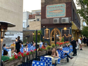 People dine and drink outside the American Sardine Bar in the Point Breeze section of Philadelphia while sitting on vibrant blue-and-white patterned chairs.