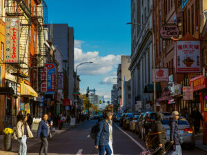 People walking across the street, with storefronts on either side and blue sky, in Philadelphia's Chinatown neighborhood