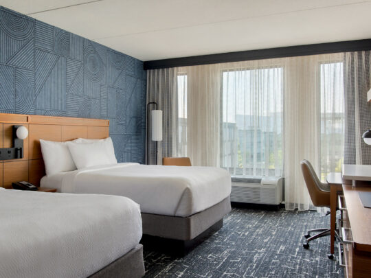 A brightly lit hotel room featuring blue carpets and walls, with two full sized beds at the Courtyard Philadelphia South at The Navy Yard