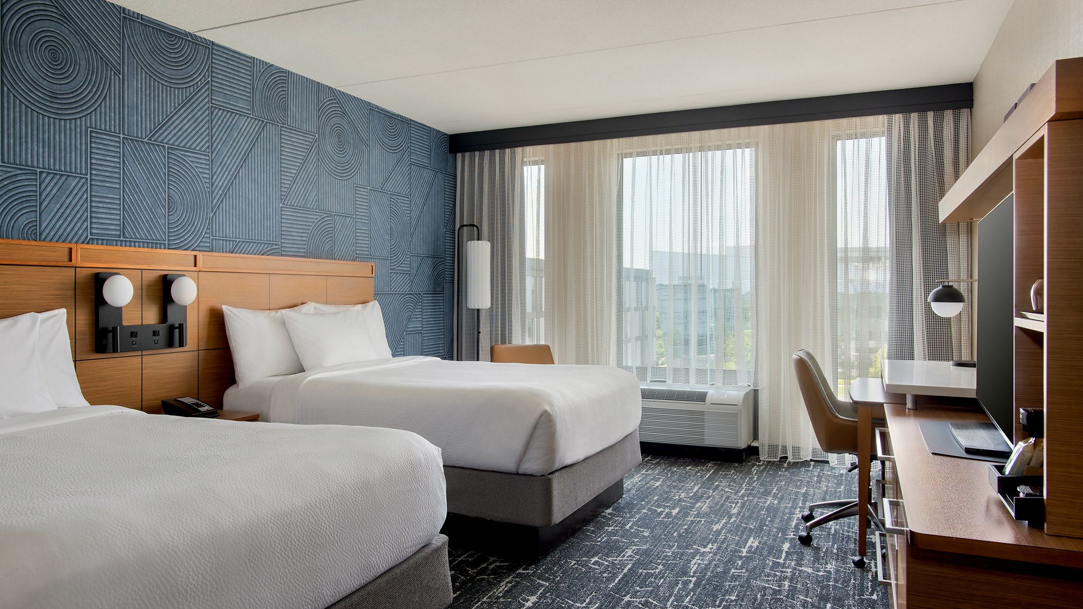 Een helder verlichte hotelkamer met blauwe tapijten en muren, met twee tweepersoonsbedden in het Courtyard Philadelphia South at The Navy Yard