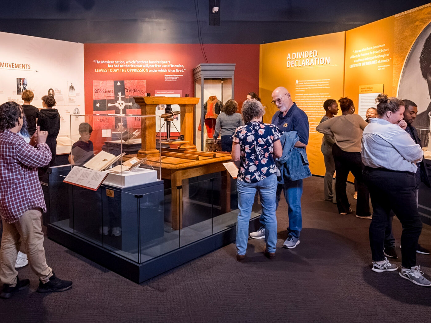 Visitors explore 'The Declaration's Journey' exhibition at the Museum of the American Revolution, examining displays about Independence Movements and A Divided Declaration with interactive exhibits and historical artifacts.