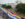 A large rainbow pride flag stretches down a street during Delco Pride in Delaware County, Pennsylvania, as crowds gather outside a historic courthouse building on an overcast day. The aerial view shows people lining the sidewalks and participating in the Pride celebration.