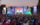 Large crowd gathered in front of a colorful stage at the FIFA World Cup 2026 Fan Festival in Philadelphia, with fans holding up phones and flags as a soccer match plays on a giant central screen.
