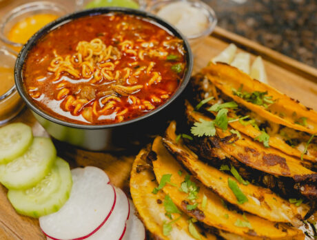 En «La Catrachita Taquería», los tacos se sirven en una mesa junto a verduras frescas y una sopa de ramen con birria