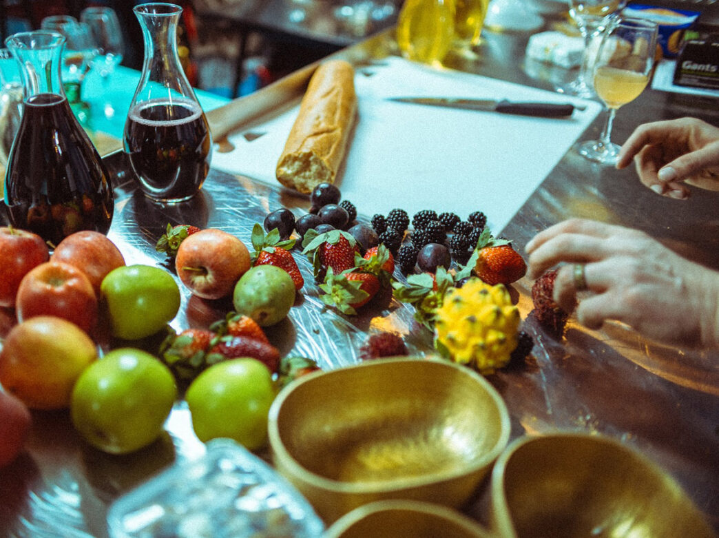 Fruit including blackberries, strawberries, apples, and dragonfruit, wine carafes, and a baguette on a table in the kitchen at LeoFigs in Fishtown.
