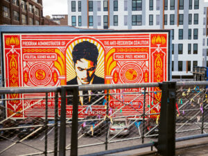 A bold red and yellow mural with a portrait and decorative patterns at The Rail Park in Philadelphia, with modern buildings in the background.