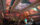 A group of visitors gather in the ornate Hall at Ministry of Awe in Philadelphia, gazing upward at an immersive ceiling installation. The historic beamed ceiling displays vibrant projected imagery in oranges, pinks, purples, and blues, creating an awe-inspiring visual experience. Architectural details include decorative molding and arched doorways, while ambient lighting enhances the contemplative atmosphere.
