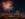 Fireworks burst over the Benjamin Franklin Parkway and Center City Philadelphia skyline during a Fourth of July celebration at night. The illuminated Philadelphia Museum of Art and city skyscrapers are visible beneath colorful fireworks lighting up the sky.