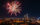 Fireworks burst over the Benjamin Franklin Parkway and Center City Philadelphia skyline during a Fourth of July celebration at night. The illuminated Philadelphia Museum of Art and city skyscrapers are visible beneath colorful fireworks lighting up the sky.