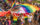 Participants march through Philadelphia’s Pride celebration carrying large rainbow and LGBTQ+ pride flags, surrounded by a dense crowd of spectators and marchers in colorful clothing and accessories.