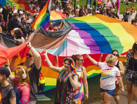 Los participantes desfilan por la celebración del Orgullo de Filadelfia portando grandes banderas arcoíris y del Orgullo LGBTQ+, rodeados por una densa multitud de espectadores y participantes vestidos con ropa y accesorios de colores.