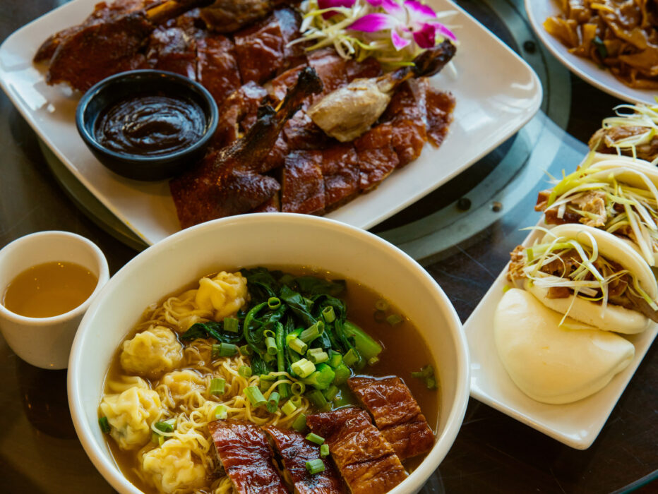 Une table pleine de cuisine asiatique, comprenant une assiette de canard rôti et un bol de soupe de nouilles wonton au Sang Kee Peking Duck House.