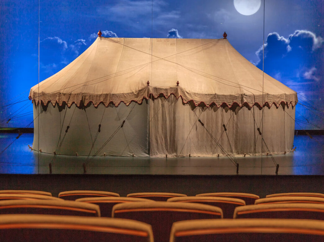 George Washington's war tent on display at a museum, shown as a large cream-colored canvas structure with period details against a theatrical backdrop.