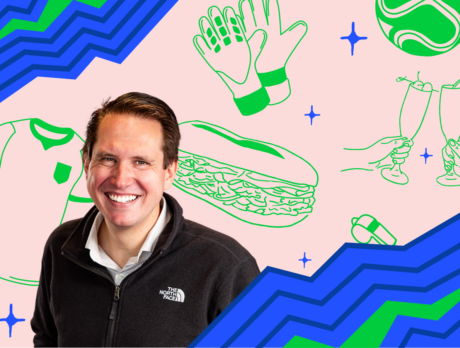 Visit Philadelphia's resident FIFA World Cup 26 expert Andrew Zwarych poses against a graphic background featuring Philadelphia-themed illustrations, including a hoagie, sports gloves, a soccer ball, and raised champagne glasses. Bold blue and green geometric patterns frame the image, creating a colorful, modern portrait.
