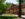 Sunlight filters through mature green trees onto the brick facade of Arch Street Meeting House, with landscaped gardens, brick walkways and historic lampposts in the foreground.
