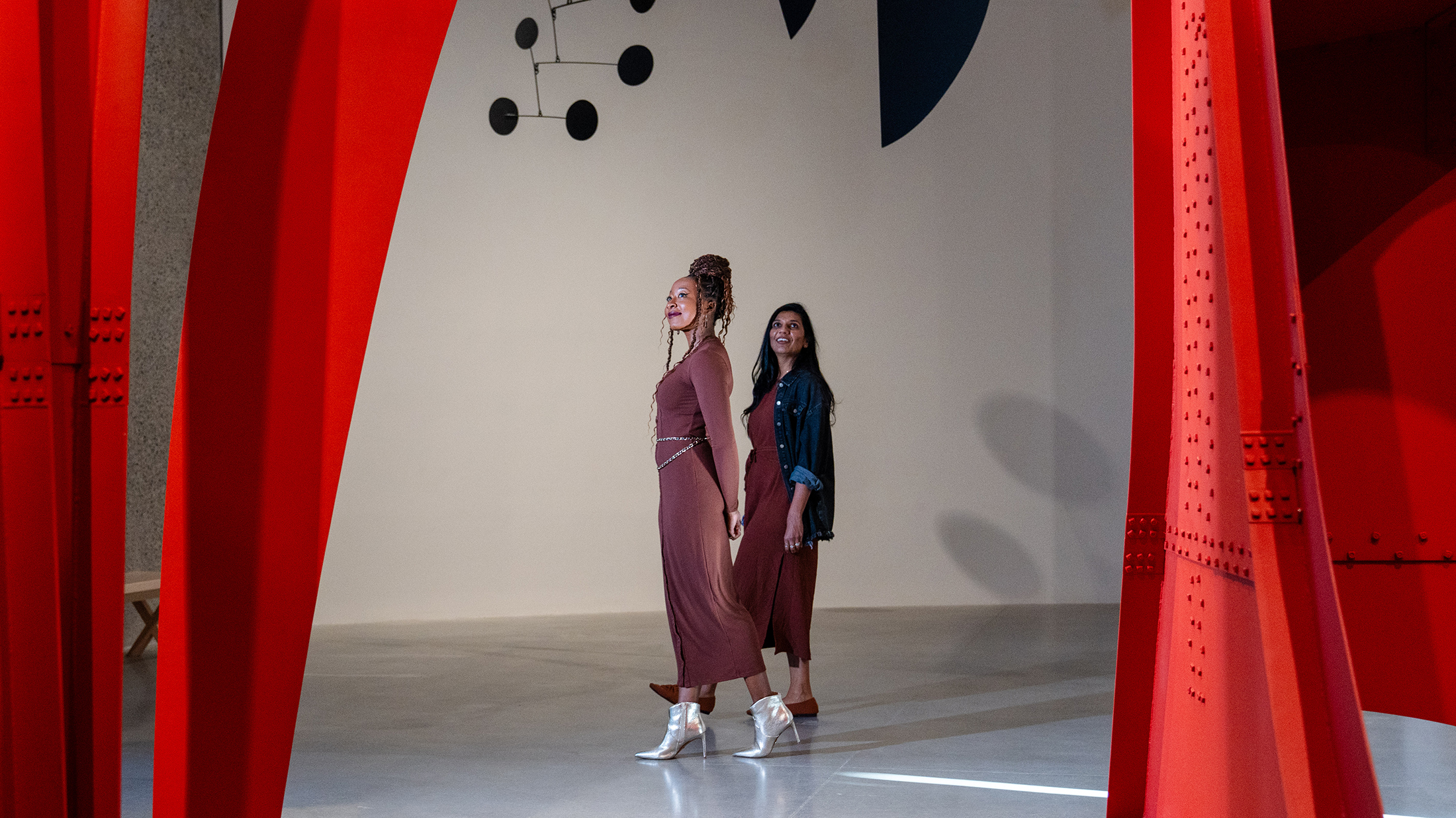 Deux visiteurs se promènent dans une salle d'exposition, encadrés par d'imposantes sculptures minimalistes rouges au sein des Jardins de Calder.