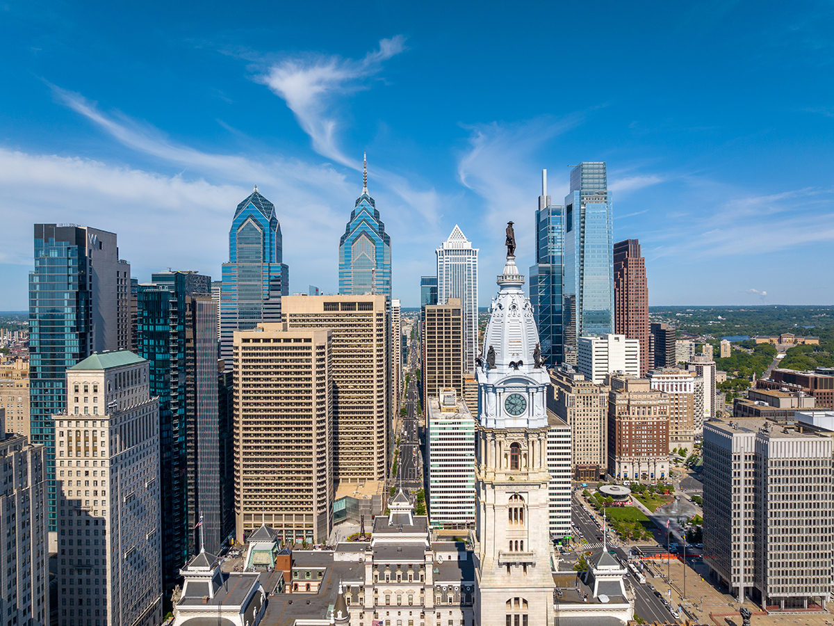 Philadelphia's Center City skyline, featuring the William Penn statue atop City Hall surrounded by modern glass skyscrapers beneath a bright blue sky.