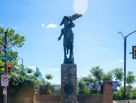 La statue en bronze du chef Tamanend trône au sommet d'un socle en pierre à l'angle des rues Front et Market à Old City ; un aigle est perché au-dessus de lui et un ciel bleu encadre le monument.