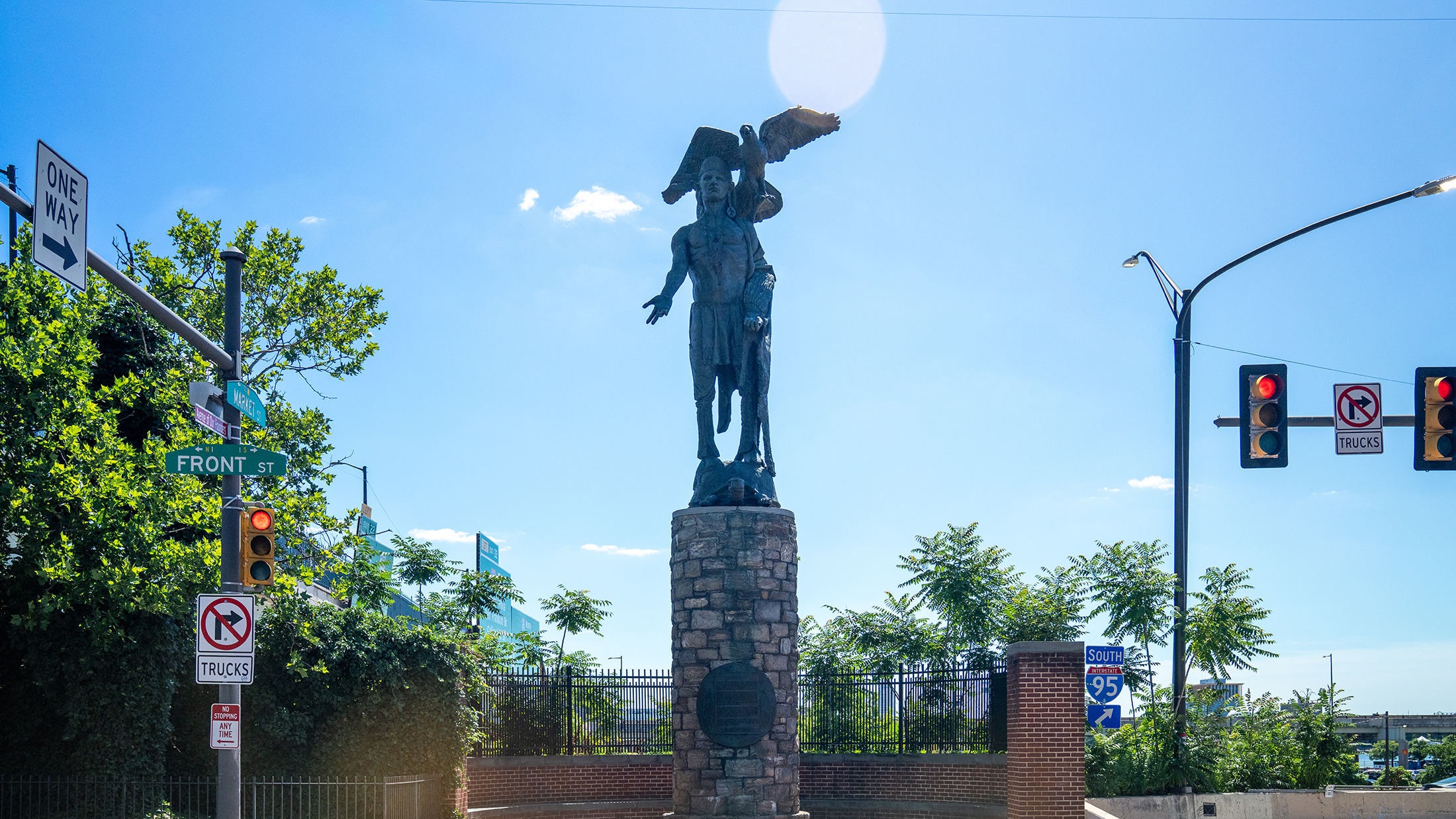 La statue en bronze du chef Tamanend trône au sommet d'un socle en pierre à l'angle des rues Front et Market à Old City ; un aigle est perché au-dessus de lui et un ciel bleu encadre le monument.