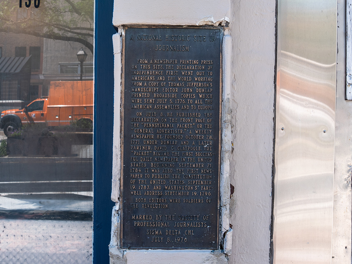 Un monument historique en bronze, commémorant l'endroit où John Dunlap a imprimé et diffusé pour la première fois la Déclaration d'indépendance, est encastré dans la façade d'un bâtiment blanc.