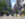 Os pedestres atravessam um cruzamento movimentado do centro da cidade ao longo da Market Street, cercados por arranha-céus, ônibus e faixas com temas da Filadélfia. O Philadelphia City Hall ergue-se ao longe, no final da rua, emoldurado por árvores e fachadas de lojas do centro da cidade.