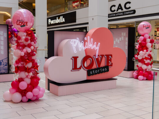 Un panneau rouge et rose à l'intérieur d'un centre commercial indique "Philly Love Stories"."
