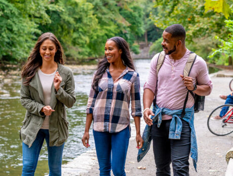 Trois personnes se promènent sur un sentier pittoresque qui longe le ruisseau Wissahickon, au milieu d'une végétation luxuriante et de bancs publics.
