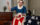 Una imitadora de Betsy Ross, vestida con ropa de la época colonial, está sentada en el interior cosiendo a mano una gran bandera estadounidense. Con un vestido azul, un delantal blanco y un pañuelo en la cabeza, cose con cuidado las franjas rojas y blancas, mientras que sobre una mesa cercana descansa un fondo azul con estrellas blancas. Los muebles de época, una vela y las ventanas con cortinas crean un ambiente histórico del siglo XVIII.