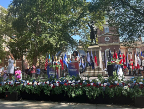 Een zanger staat op een openluchtpodium voor Independence Hall, waar patriottische bloemstukken en militaire vlaggen het podium sieren tijdens de ‘Celebration of Freedom’-ceremonie.